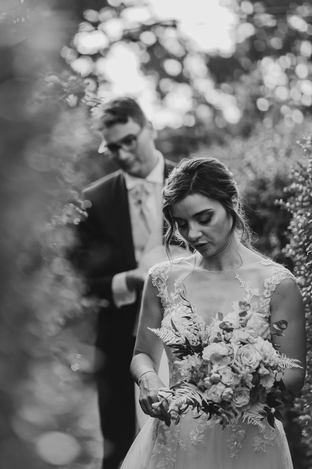 La sposa guarda il bouquet con lo sposo alle sue spalle, in bianco e nero