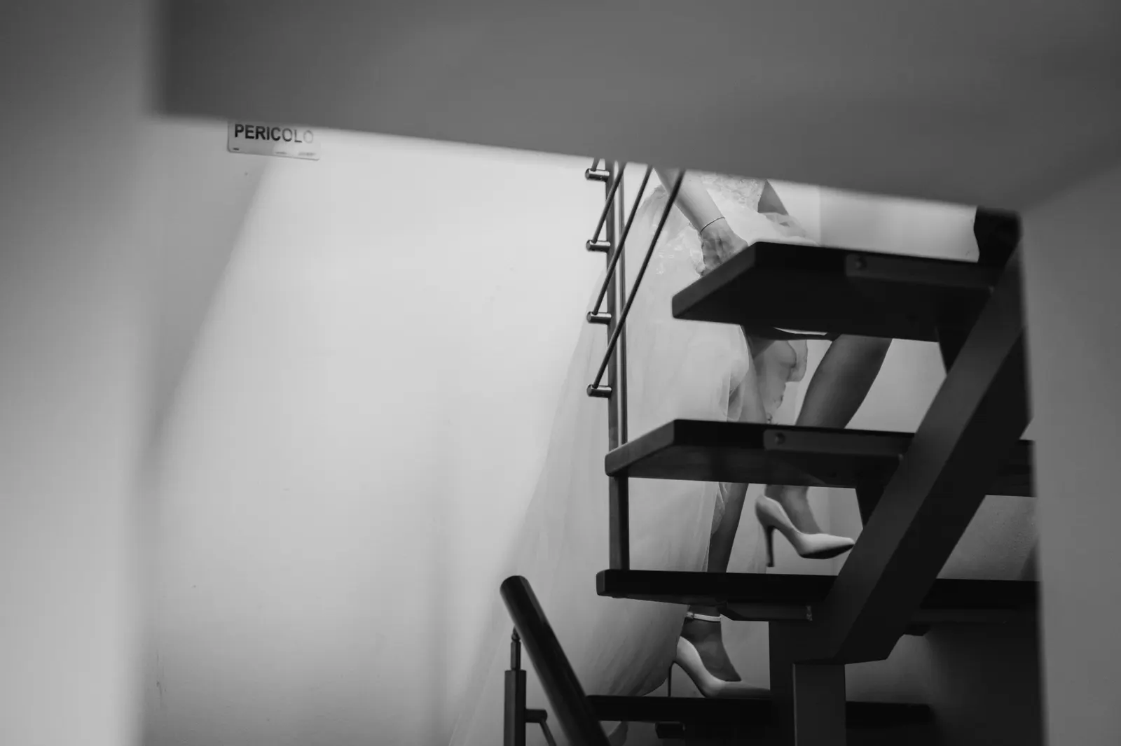 La sposa scende una scala interna: si vedono le scarpe e lo strascico, in bianco e nero