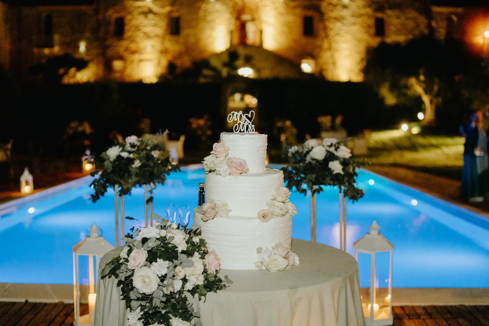 La torta nuziale a bordo piscina, con le mura del castello illuminate di sera