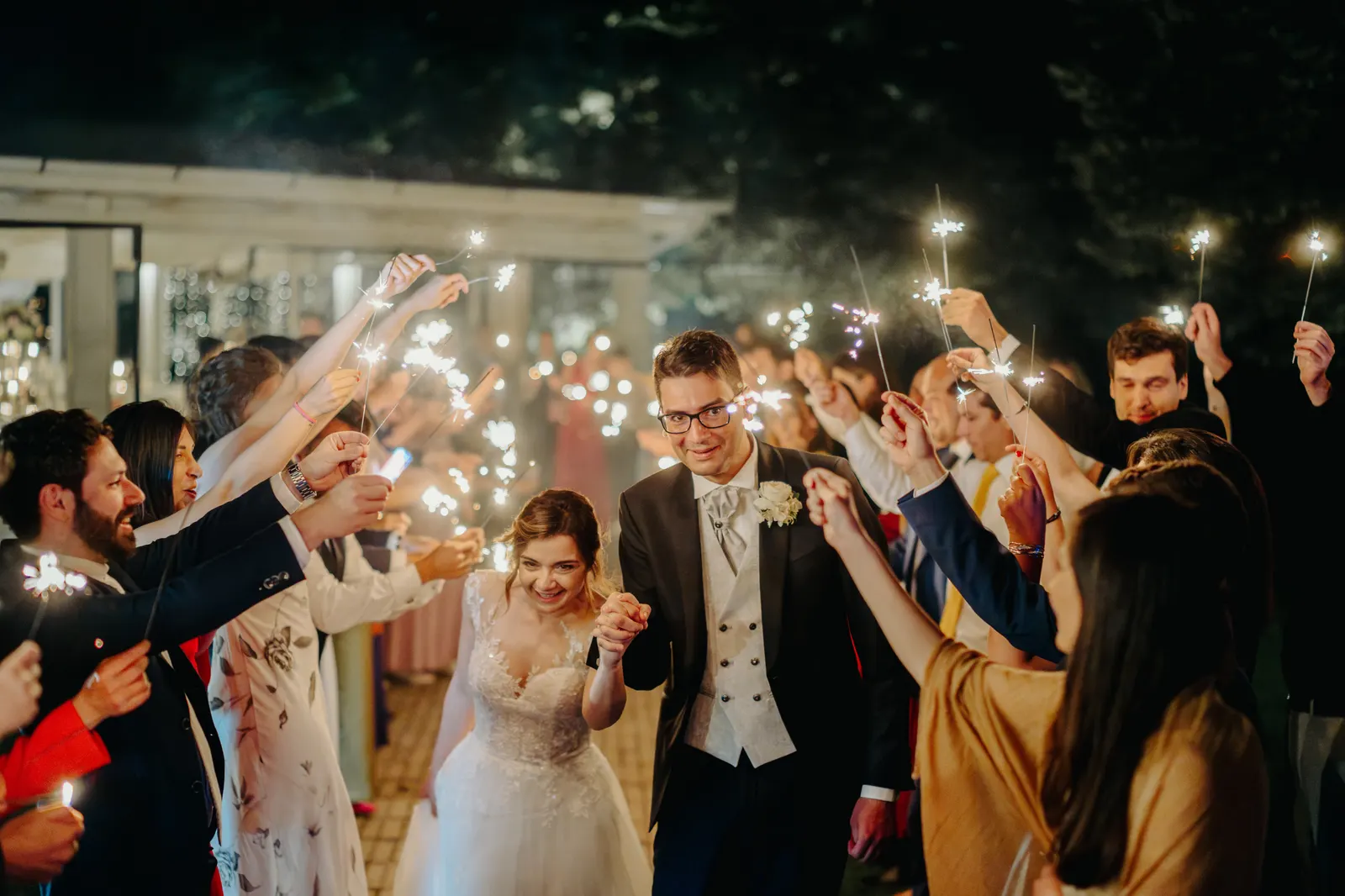Gli sposi tra gli invitati che alzano le scintille luminose, di sera