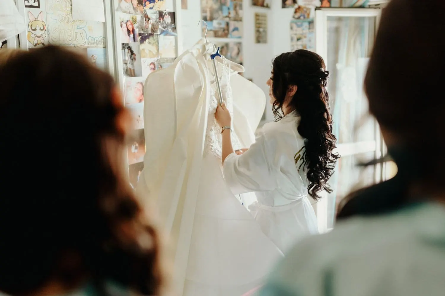 The bride in front of her dress hanging in her room