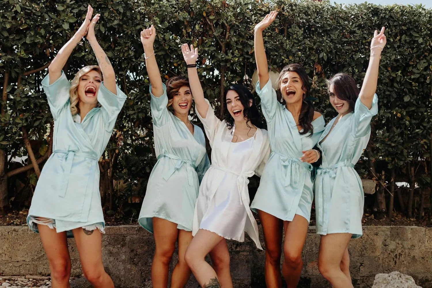 The bride and her friends in mint-green robes cheering in the garden