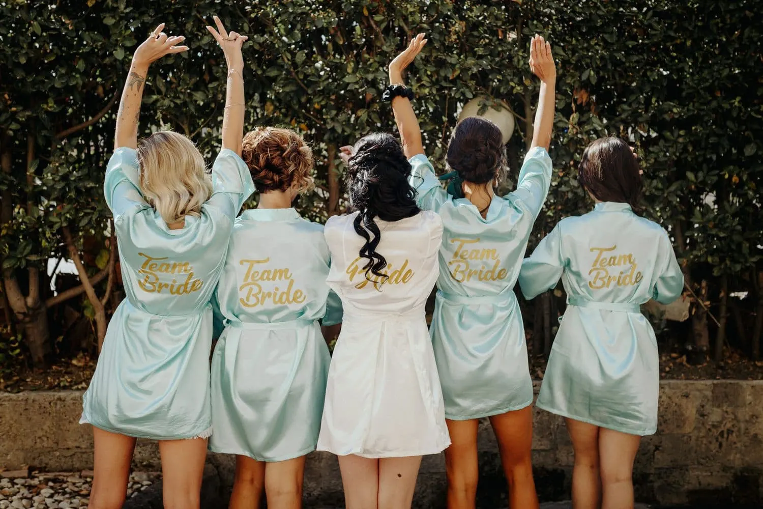 The friends seen from behind in their Team Bride robes, arms raised
