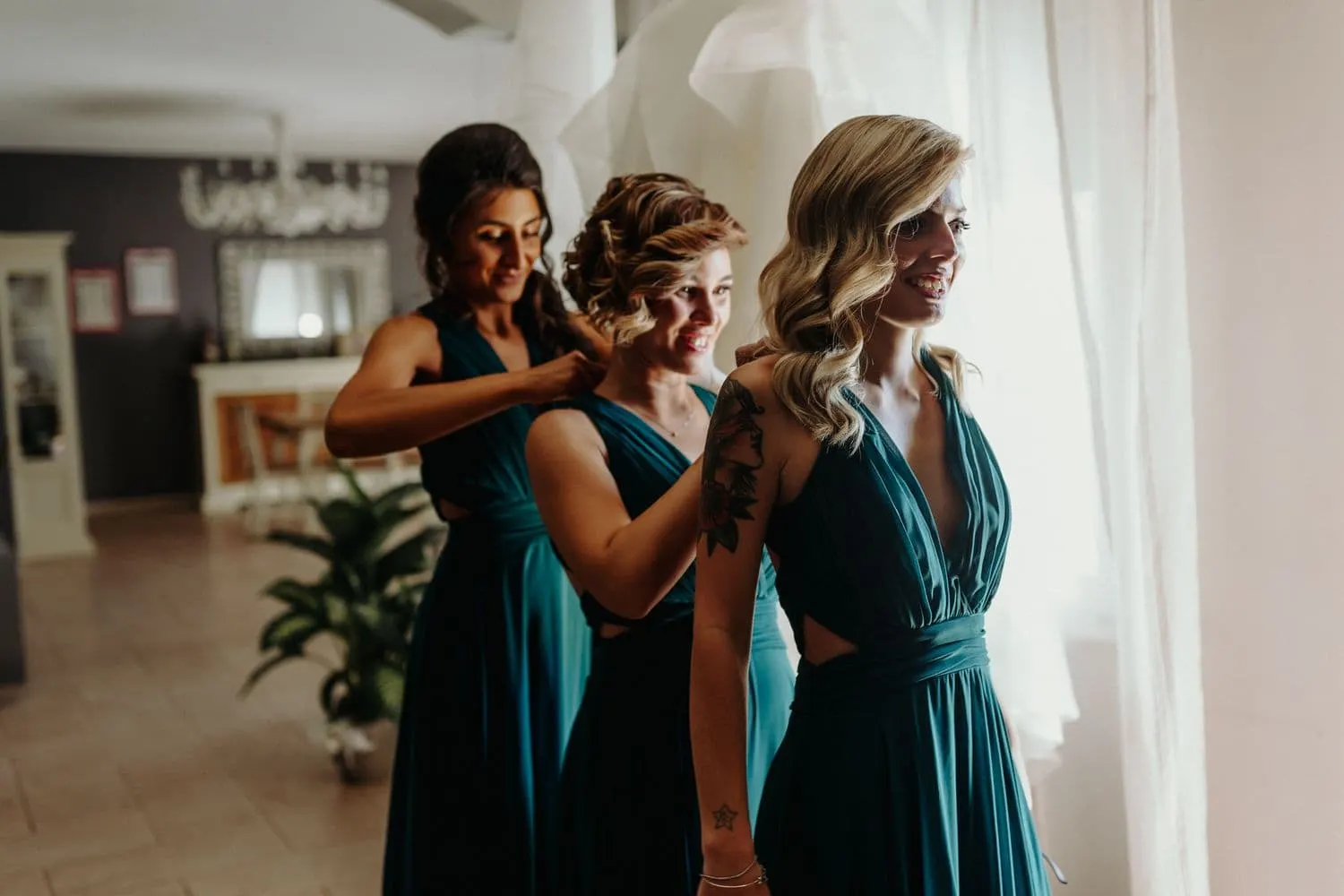 The bridesmaids helping each other fasten their forest-green dresses