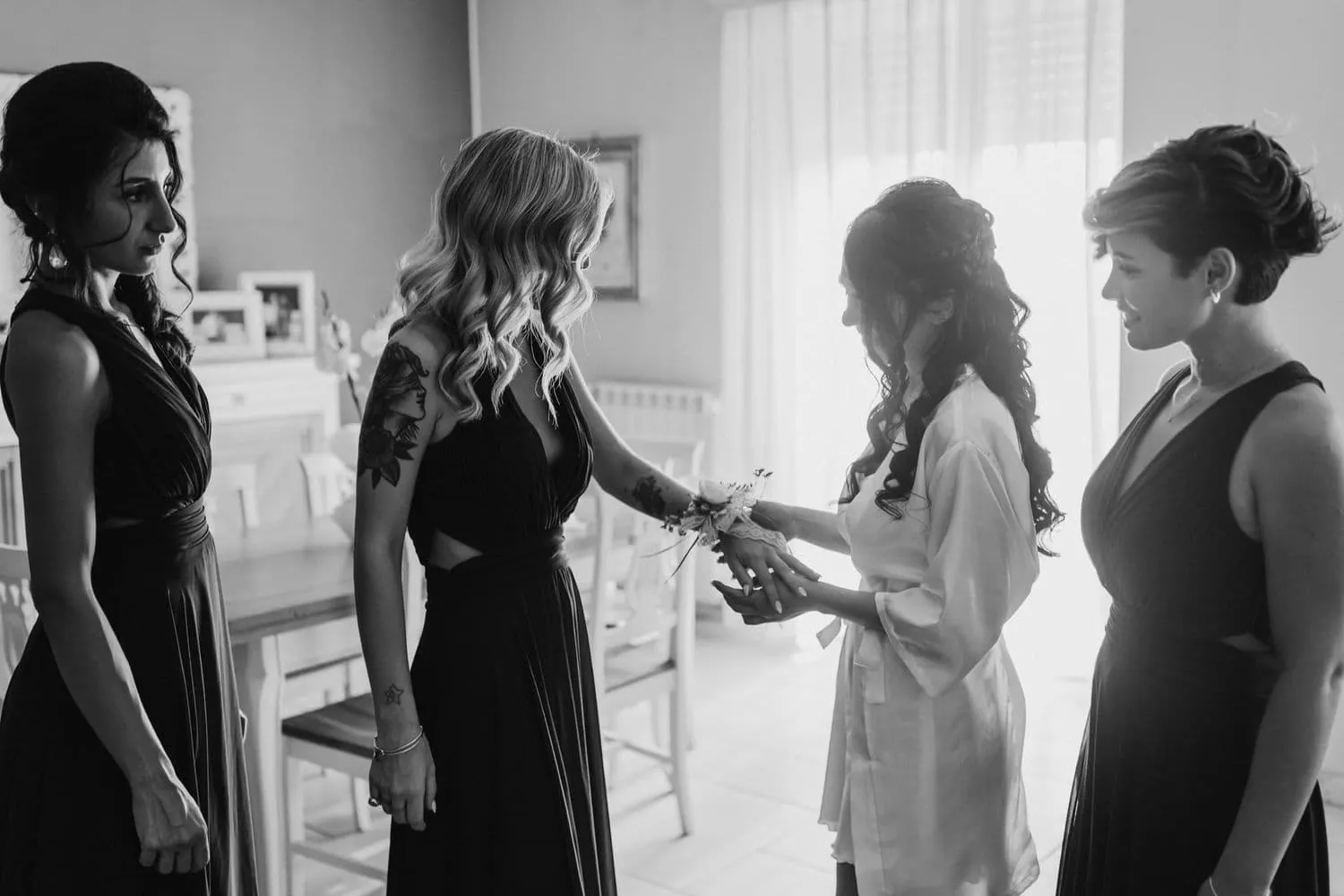 Micaela tying a flower corsage on a bridesmaid's wrist, in black and white