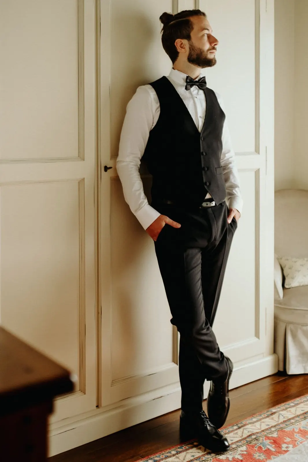 Portrait of Raffaele in black waistcoat and bow tie, leaning against the door