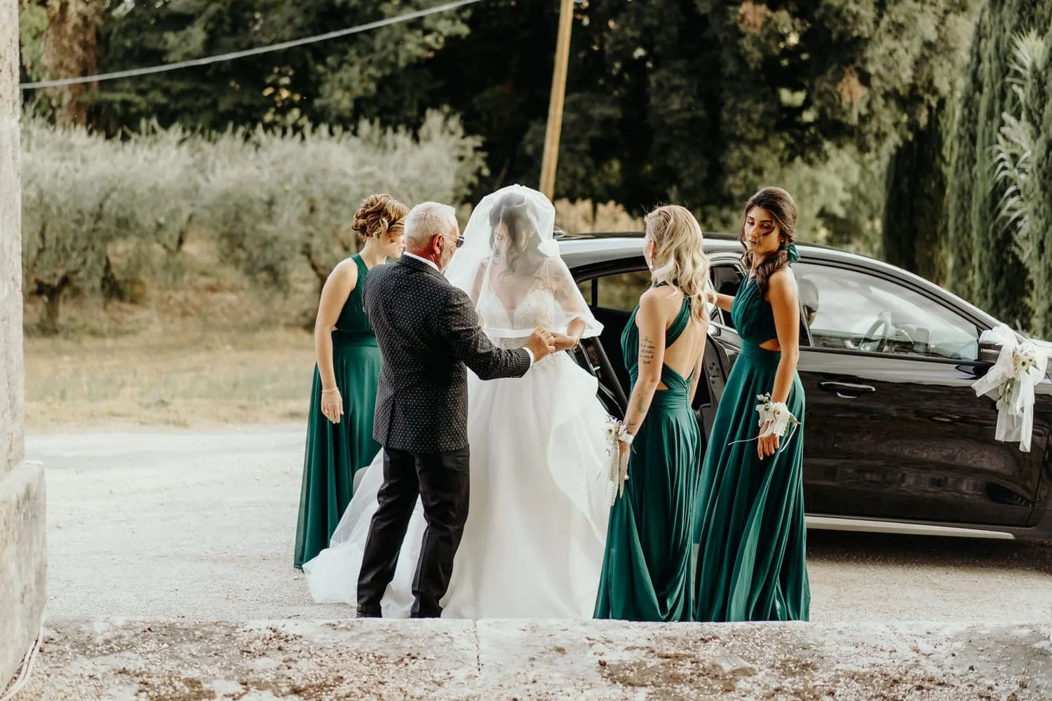 Micaela getting out of the car, helped by her father and bridesmaids