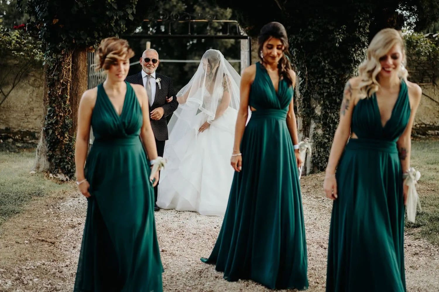 The bridesmaids in forest green walking ahead of the bride along the avenue