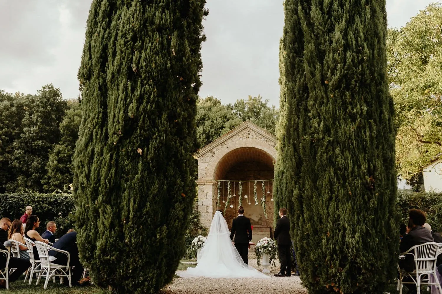 The ceremony seen from a distance between two cypresses, in front of the stone shrine