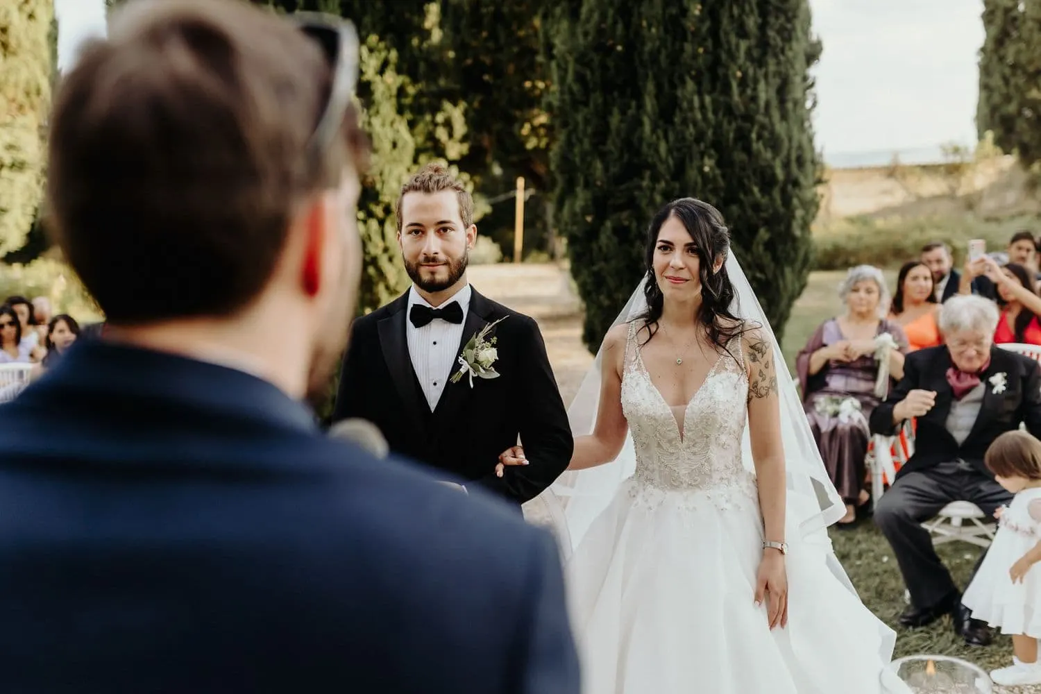 The couple listening to a friend speaking into the microphone during the ceremony