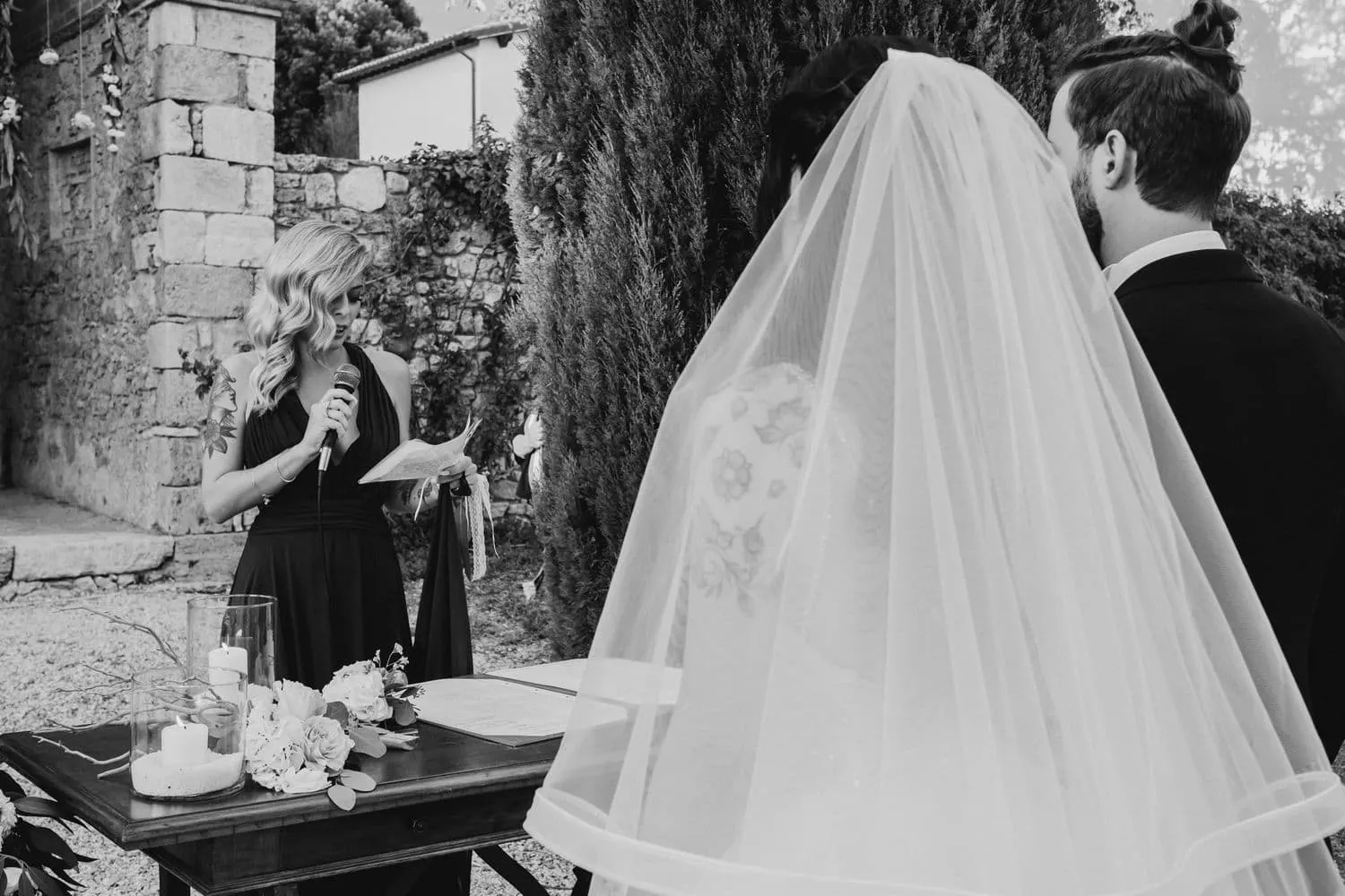 A friend reading into the microphone, with the bride's veil in the foreground, in black and white