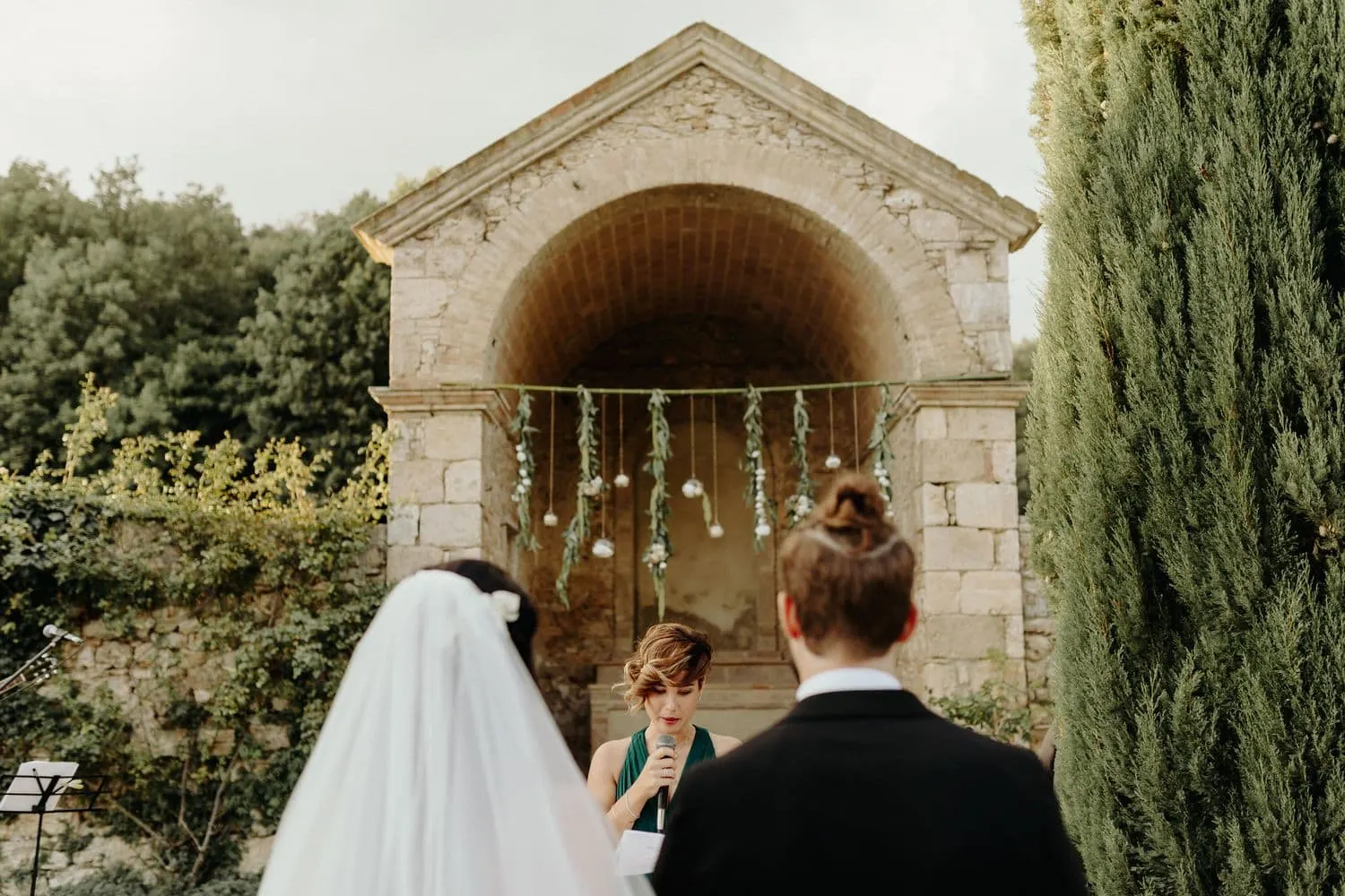 The couple seen from behind in front of the arched shrine, among the cypresses
