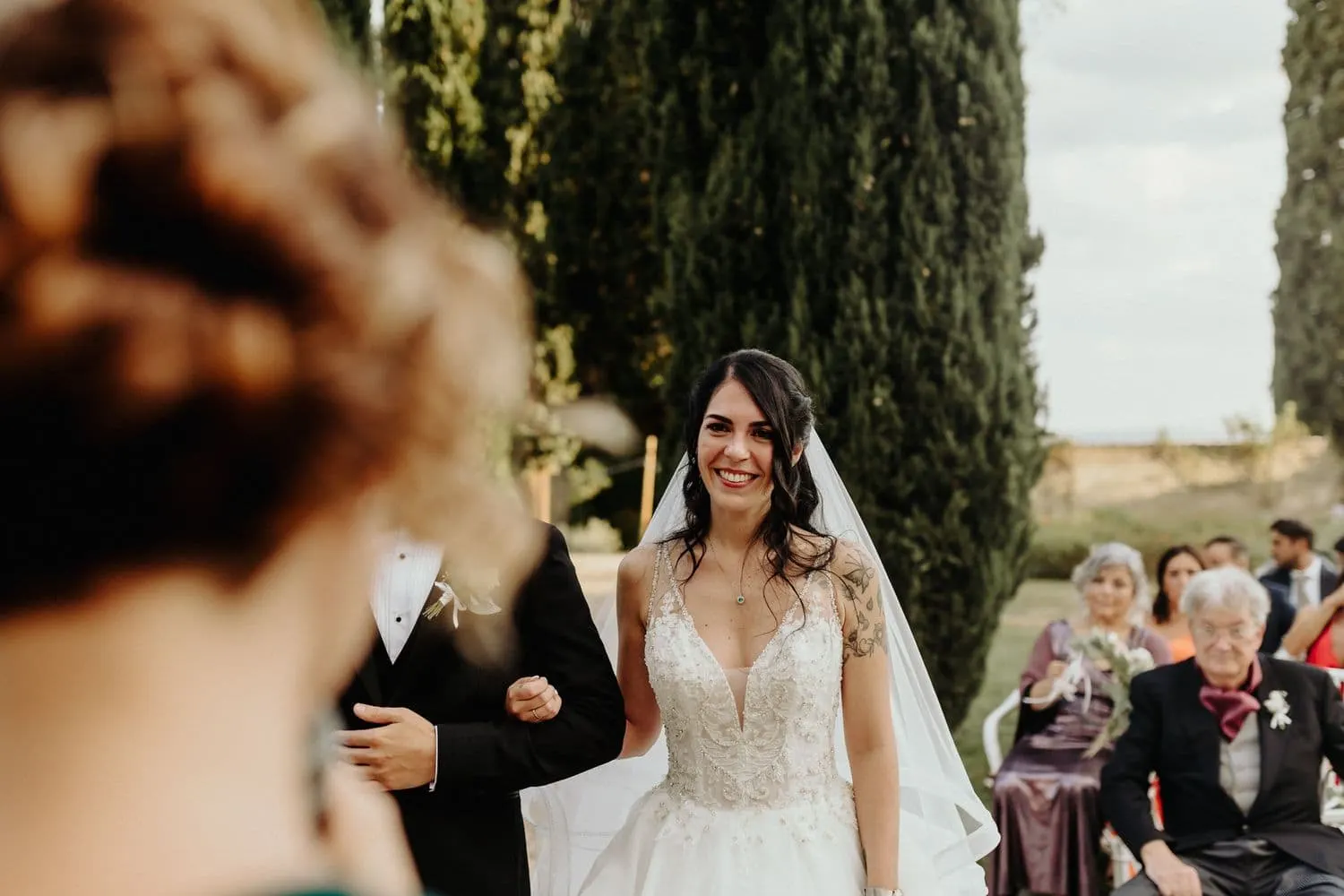 Micaela smiling among the guests, seen over a bridesmaid's shoulder