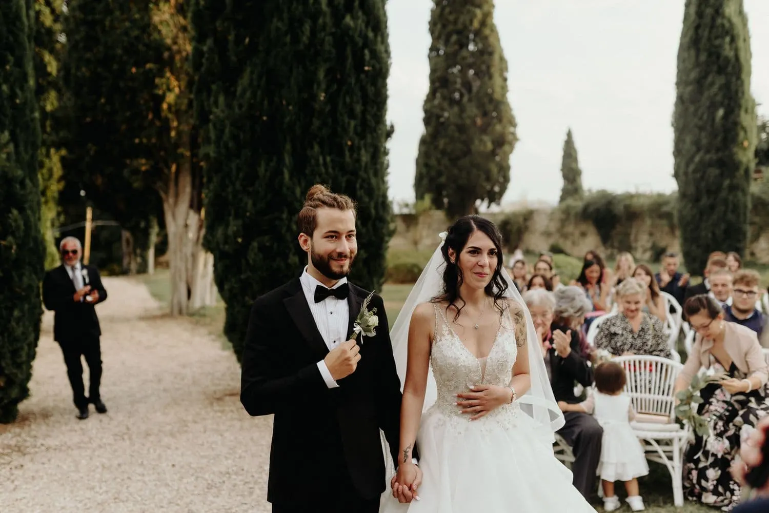 The couple standing in front of the guests along the avenue