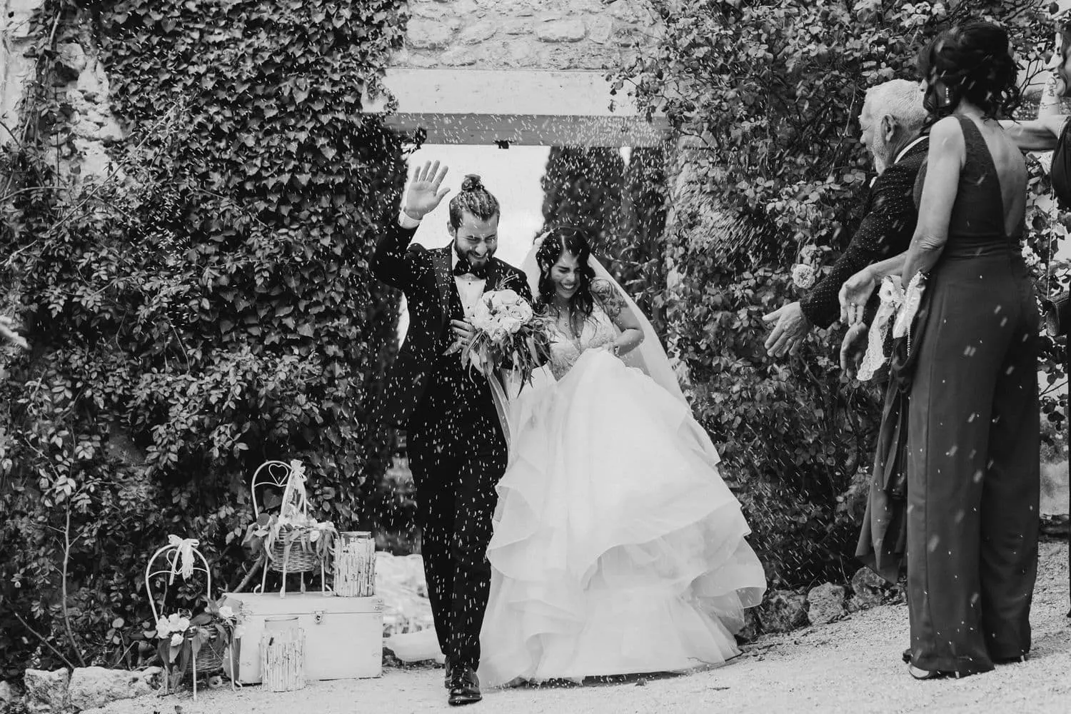 The couple walking out through thrown petals, in black and white