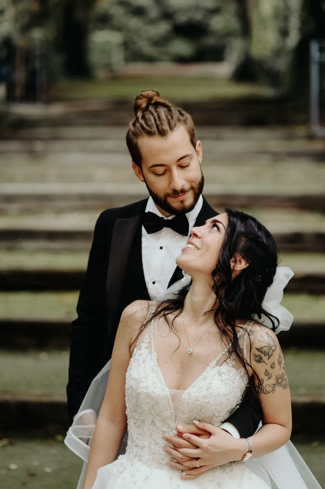 Raffaele holding Micaela from behind as she looks up at him, on the park steps