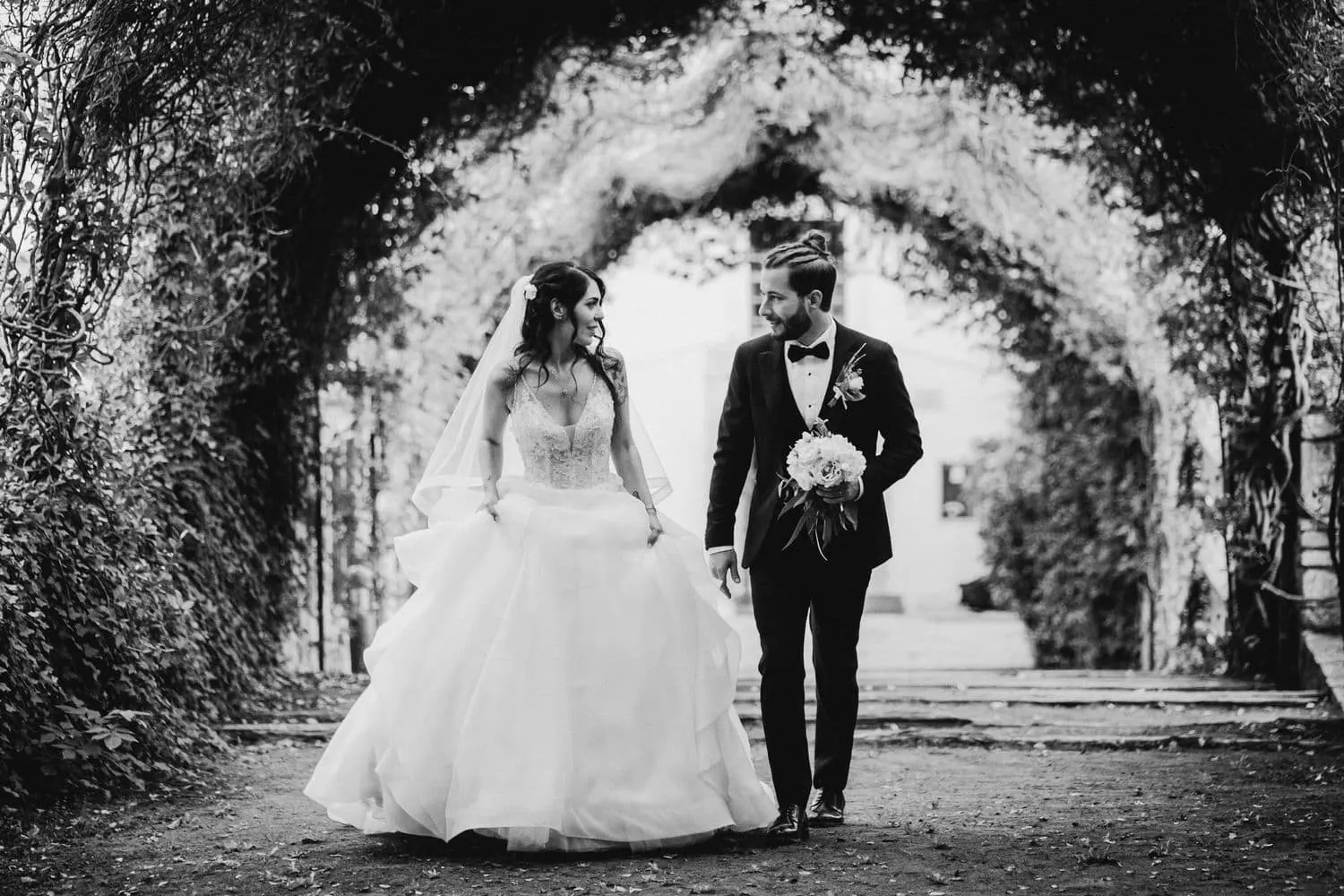 Micaela and Raffaele walking under the tunnel of trees, in black and white