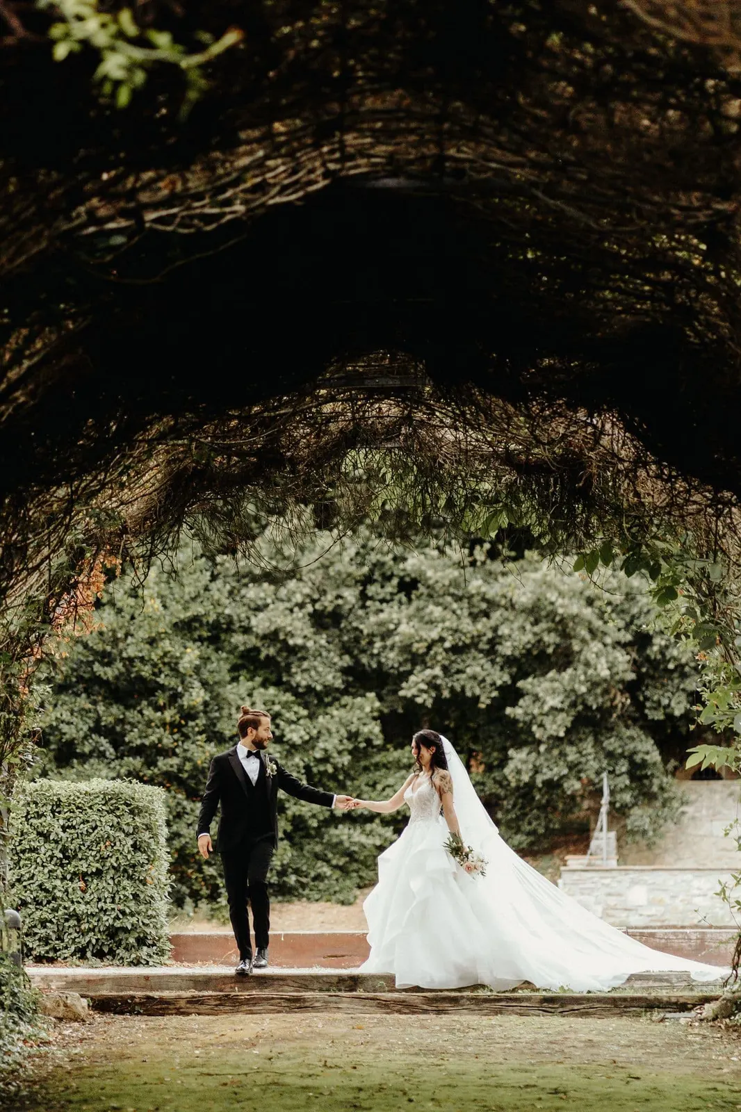 The couple holding hands on the lawn, framed by branches