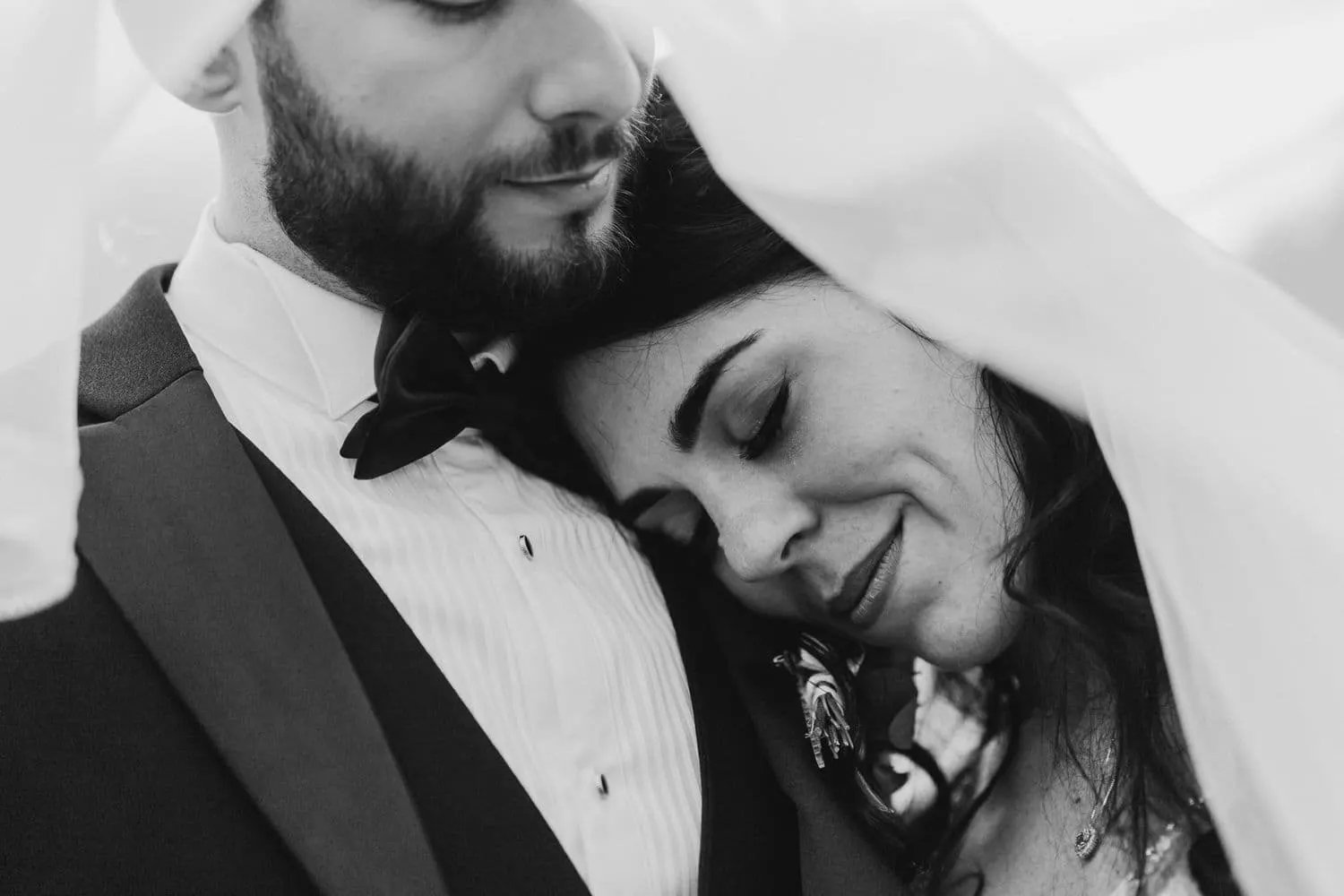 Micaela resting against Raffaele's chest under the veil, in black and white