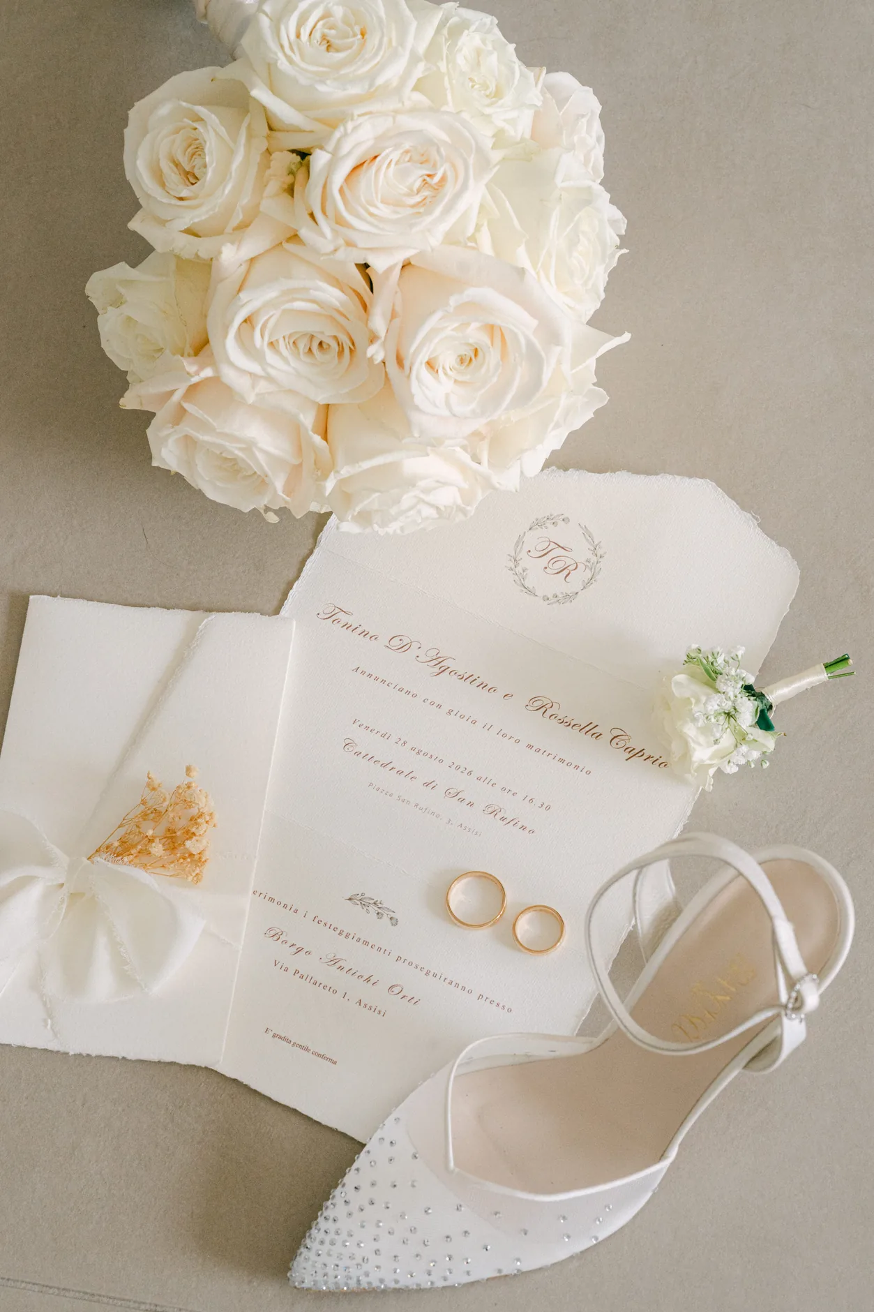 Il bouquet di rose bianche accanto alla partecipazione, alle fedi e alla scarpa della sposa