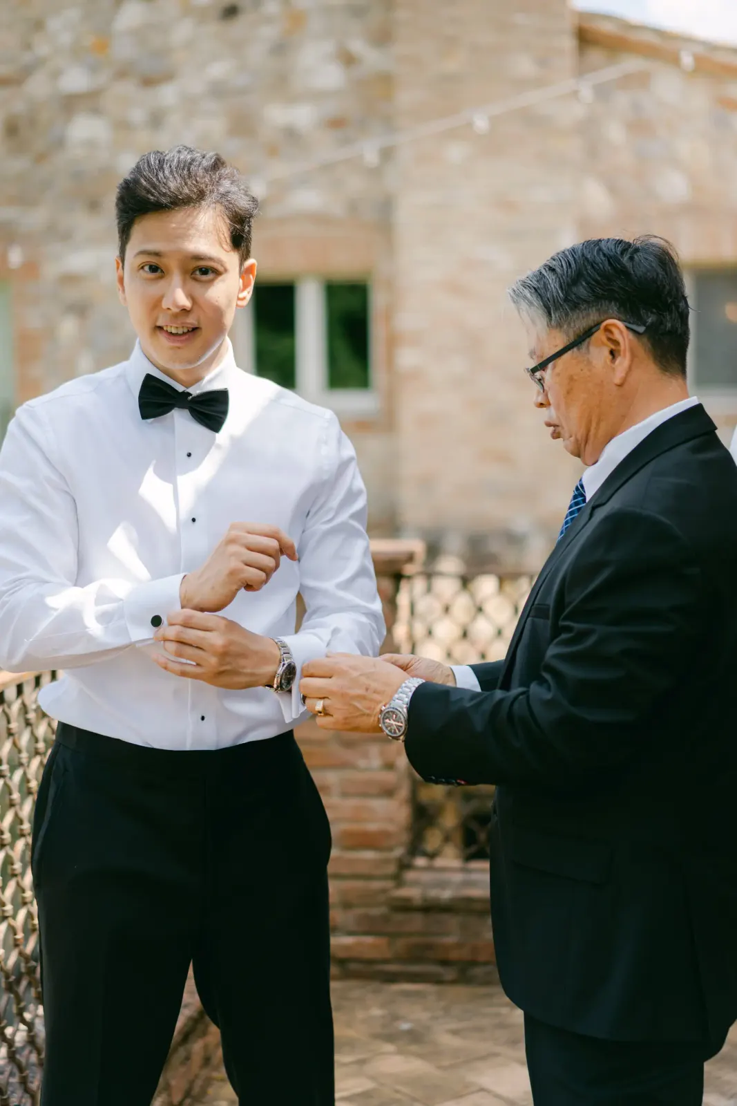 James si allaccia i polsini della camicia accanto al padre, nel cortile in pietra