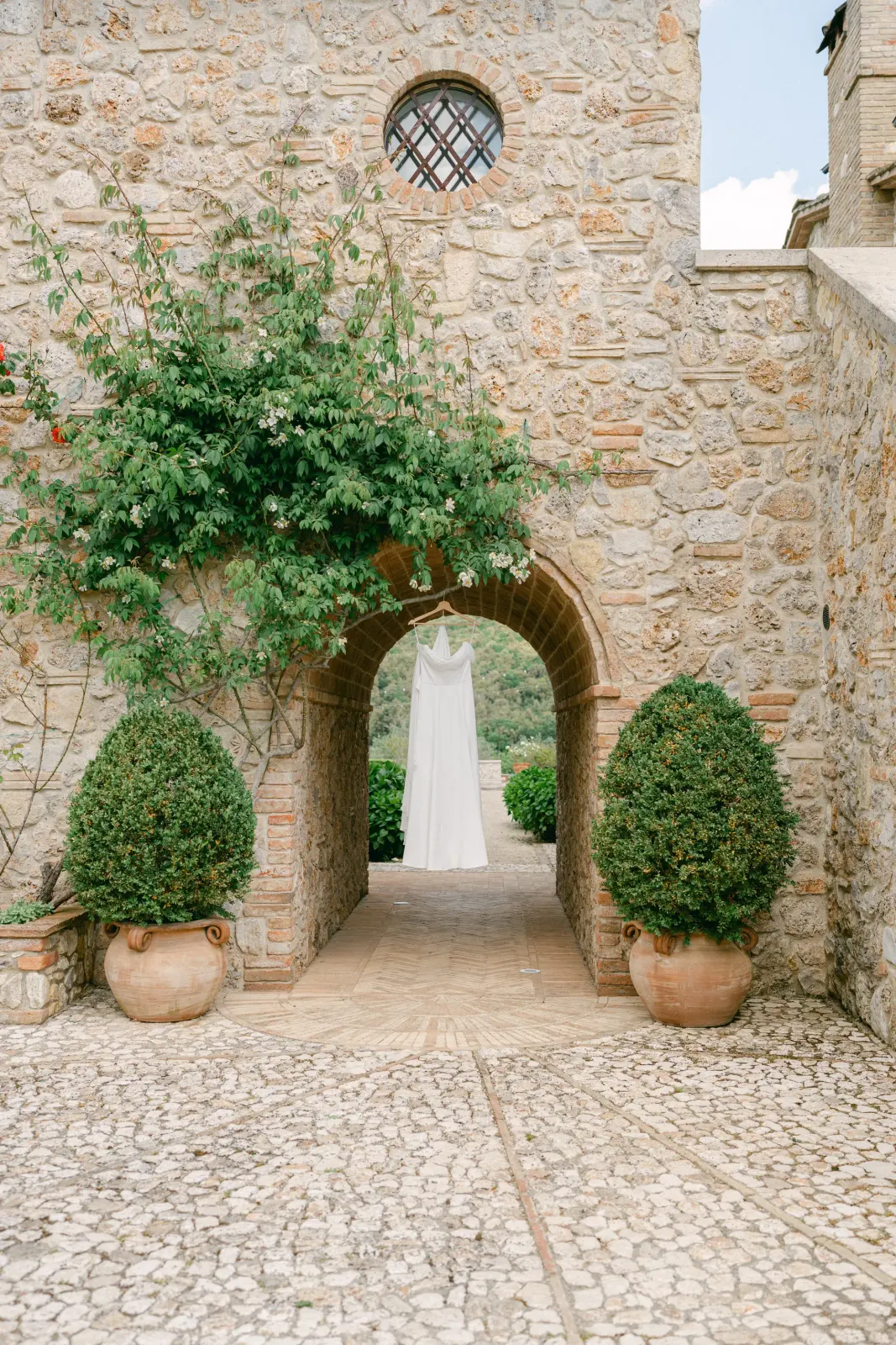 L'abito da sposa appeso sotto un arco in pietra, con il giardino della Tenuta del Gallo sullo sfondo