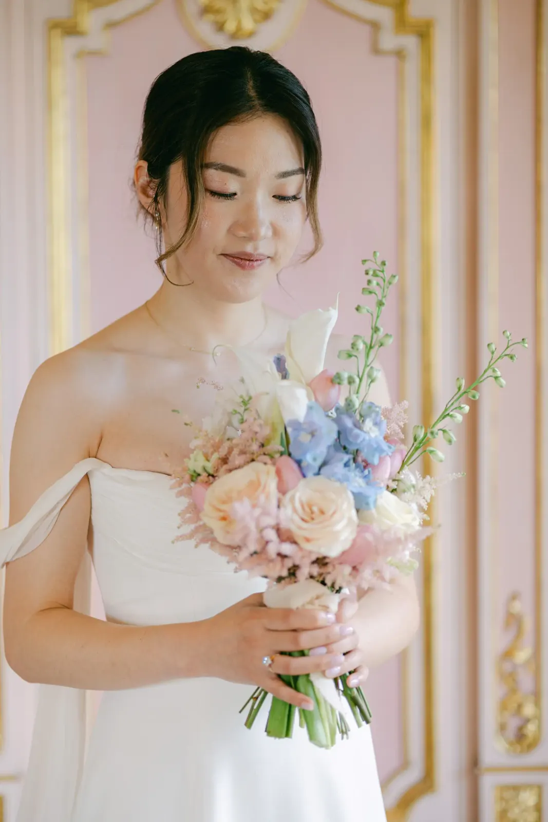 Audrey guarda il bouquet azzurro e pesca in una sala dalle pareti rosa e oro