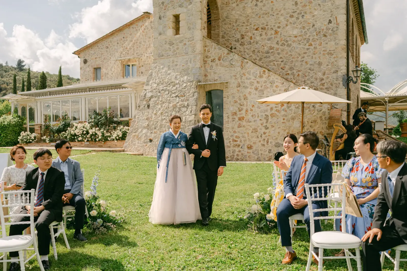 James arriva alla cerimonia al braccio della madre in hanbok, tra gli invitati seduti