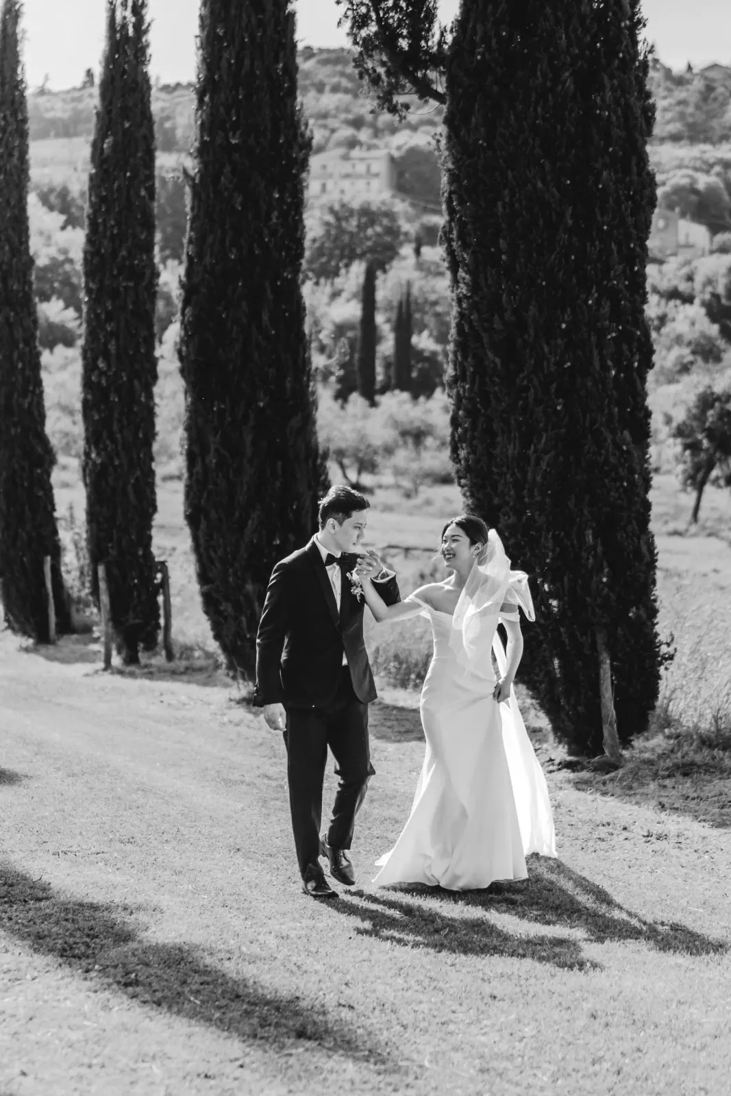 Audrey e James ridono camminando tra i cipressi, in bianco e nero