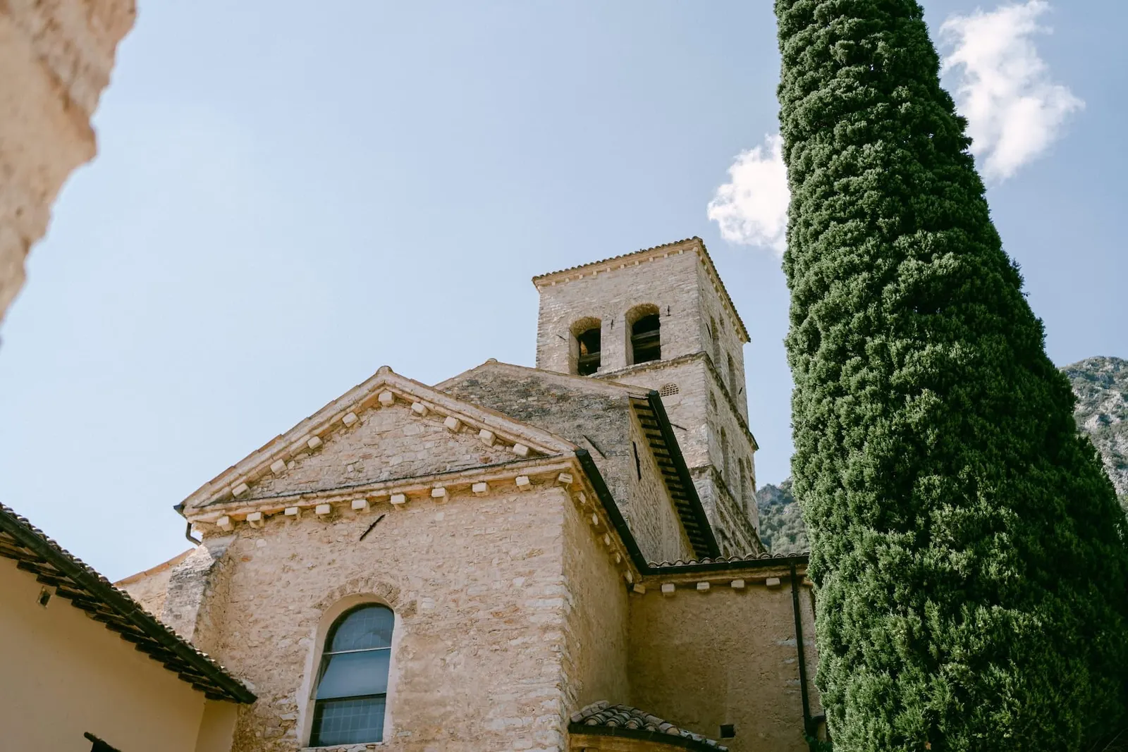 The church and bell tower of Abbazia San Pietro in Valle beside a cypress