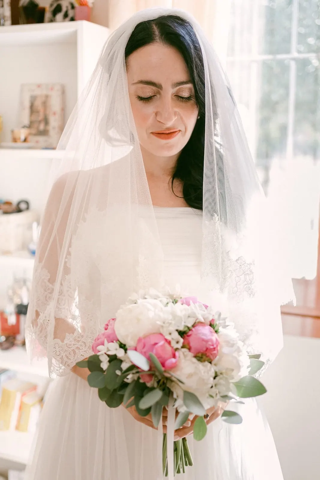 Valentina with the veil over her head and a bouquet of pink and white peonies