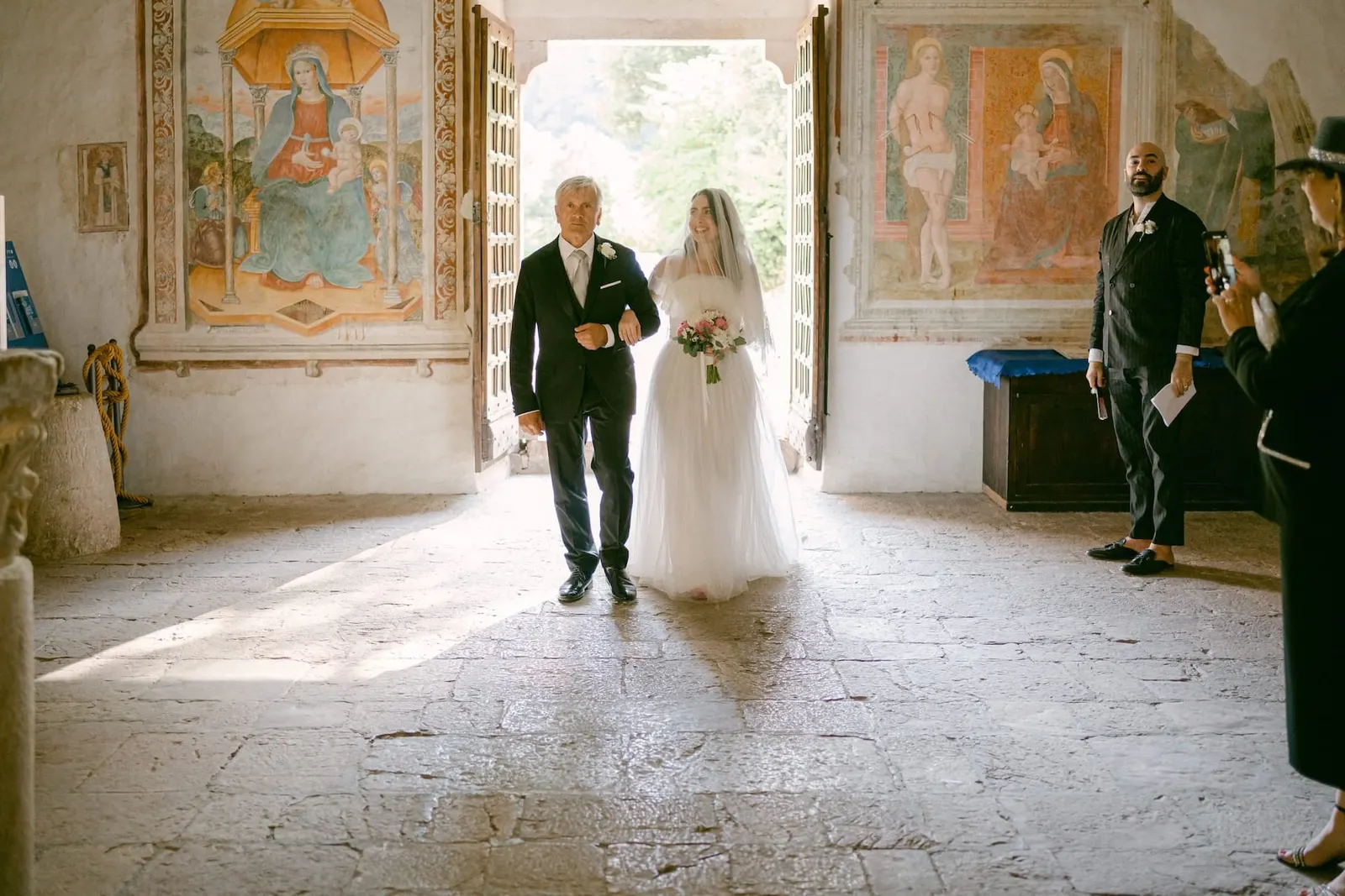 La sposa e il padre entrano in chiesa in controluce, tra gli affreschi