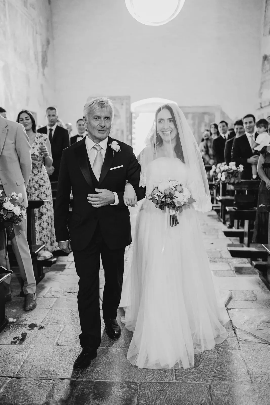 Valentina walking down the nave on her father's arm, in black and white