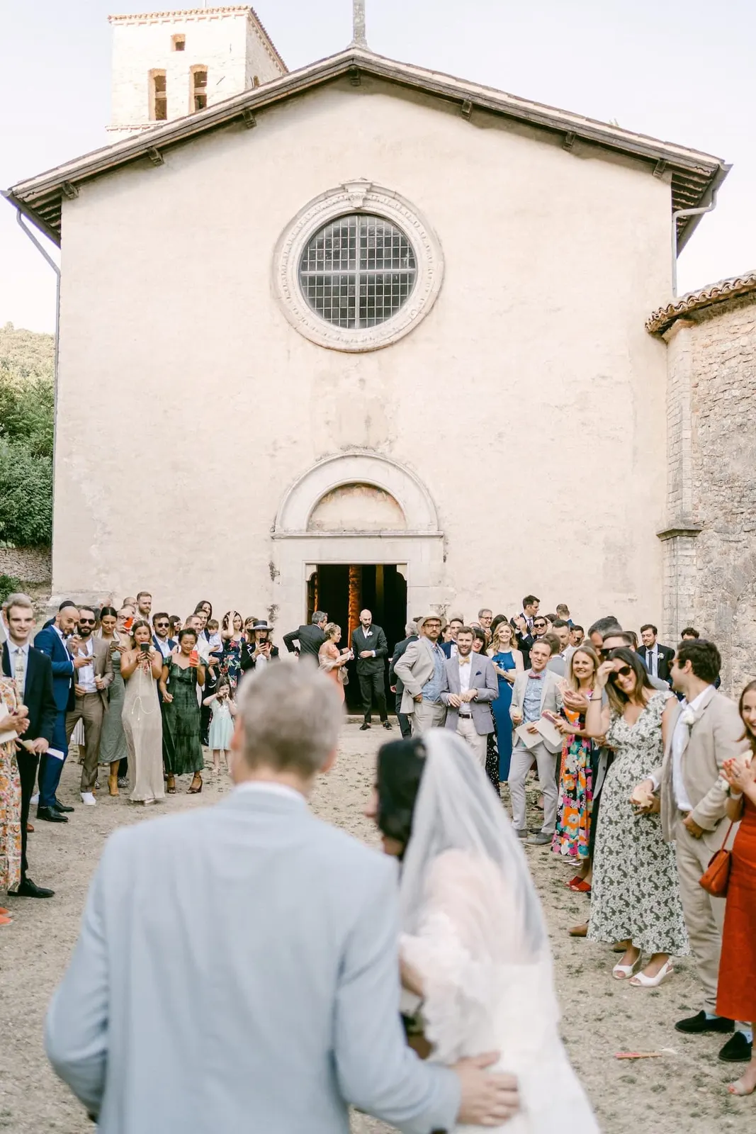 The couple seen from behind, facing the guests gathered outside the abbey church