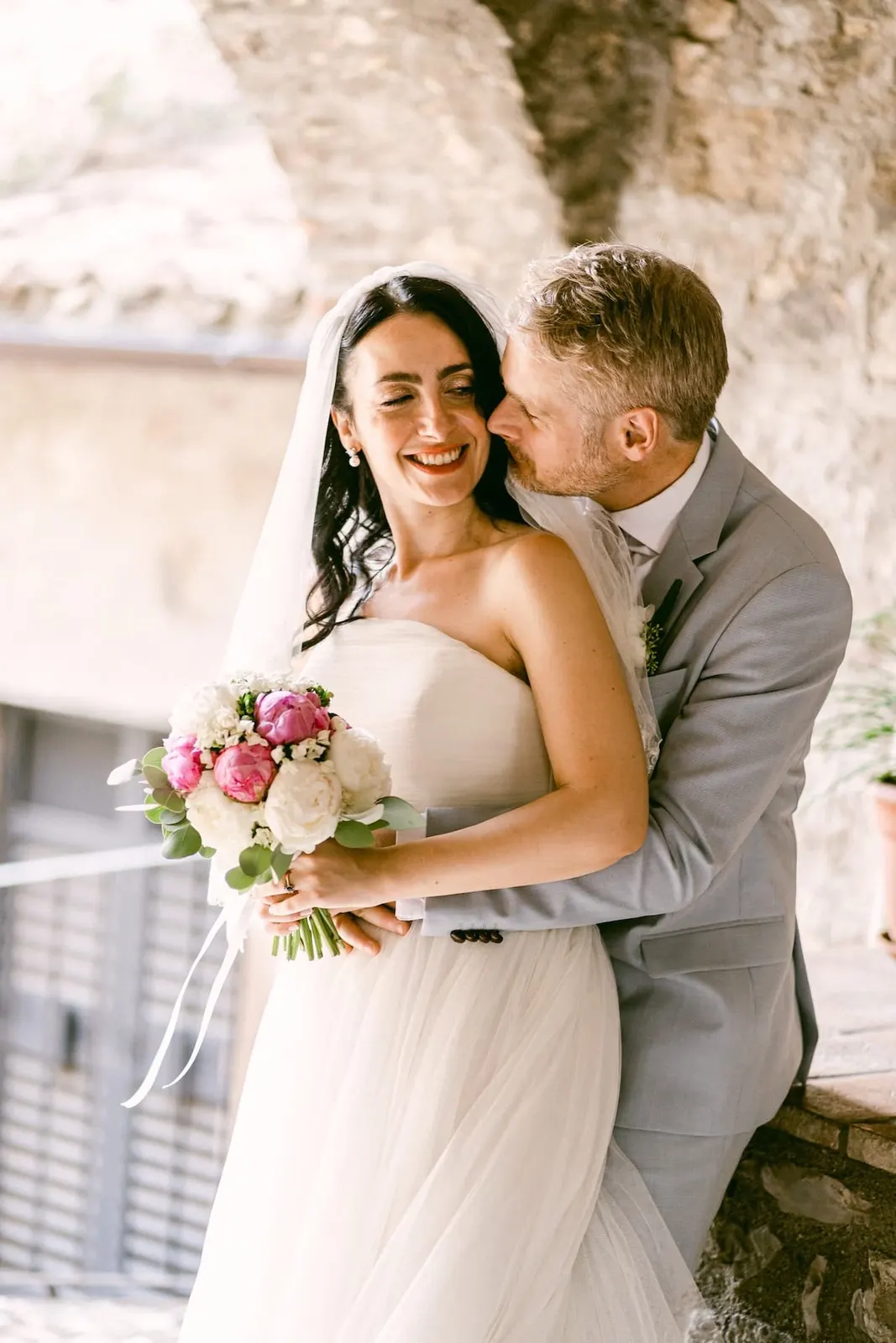 Thomas kissing Valentina on the cheek, with the stone houses behind