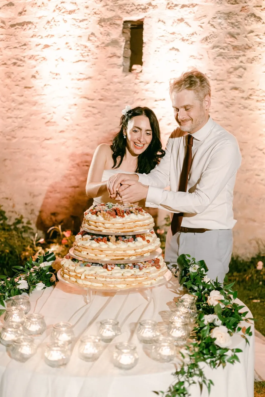 Valentina and Thomas cutting the cake against the lit wall of the abbey