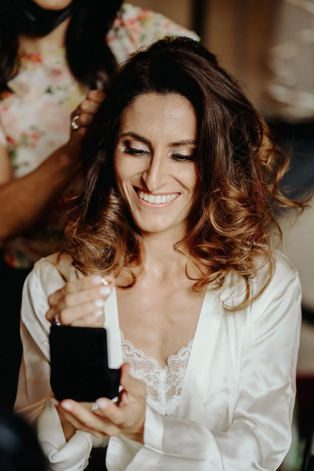 The bride laughing with a small box in her hand while her hair is styled