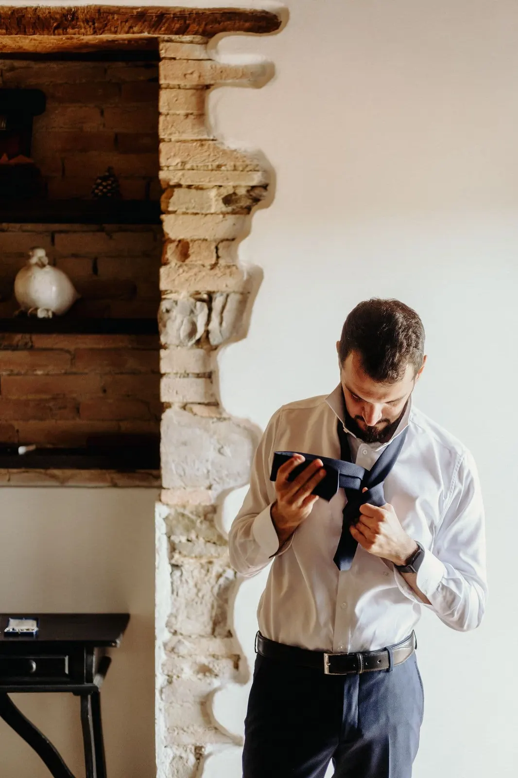 The groom knotting his tie in a room of the stone farmhouse