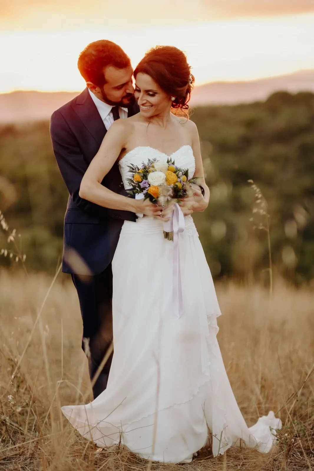 Portrait of the couple embracing in the tall grass at sunset