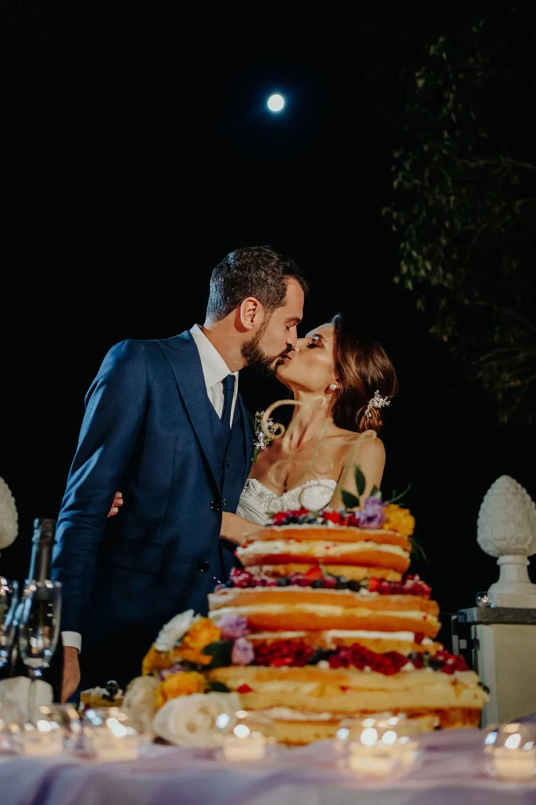 The couple kissing behind the cake, with the moon in the sky