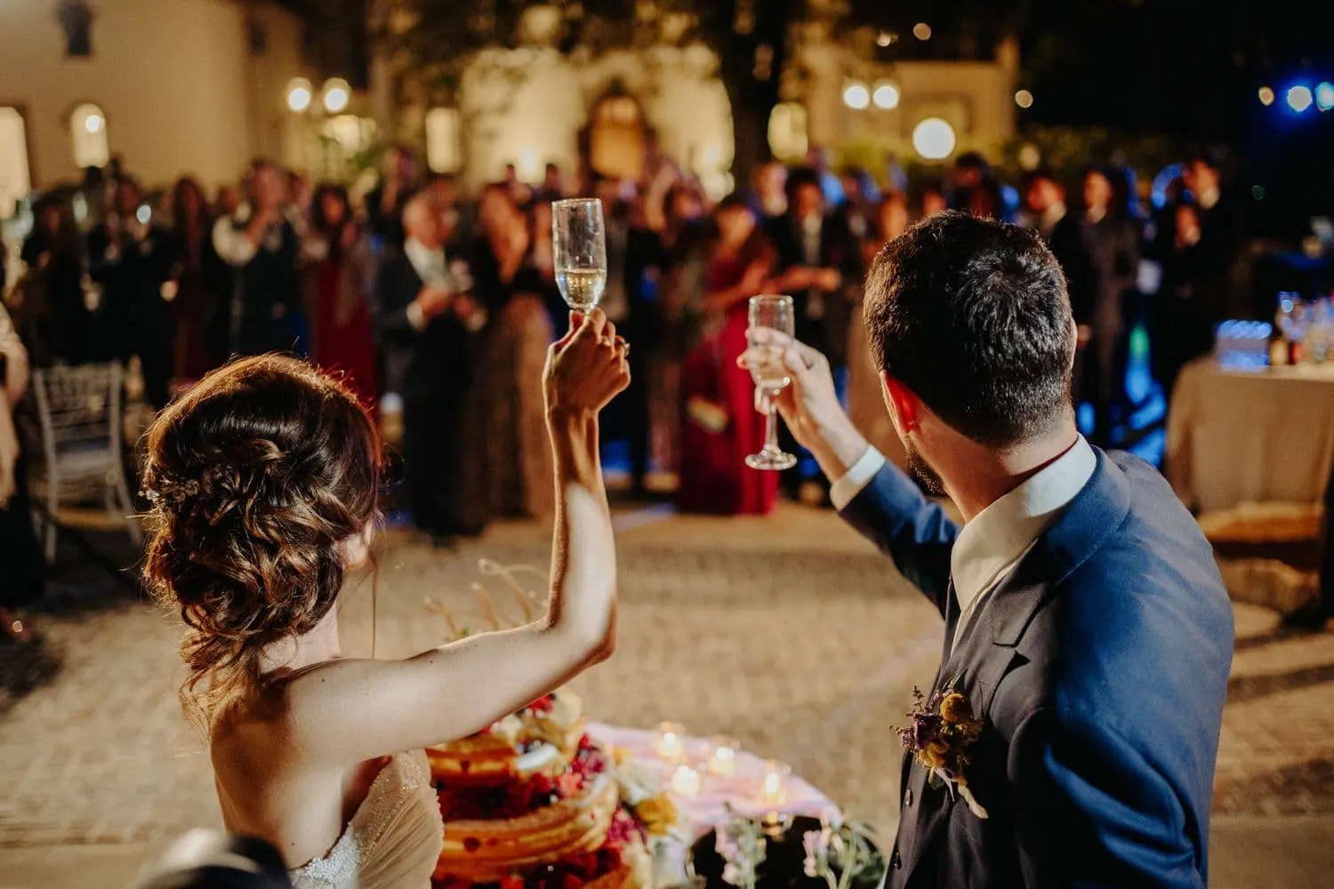 The couple raising their glasses to the guests after cutting the cake